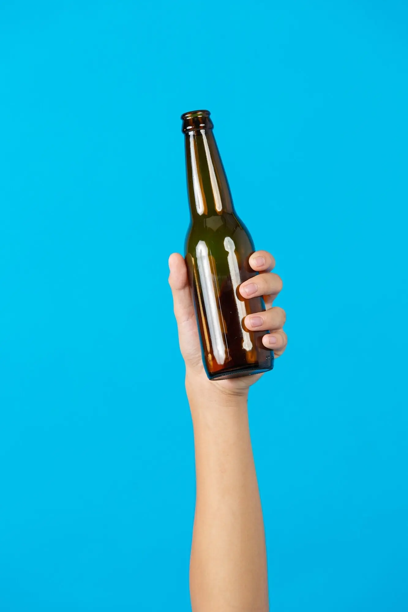 Eine Hand hält eine gebrauchte Flasche vor blauem Hintergrund.